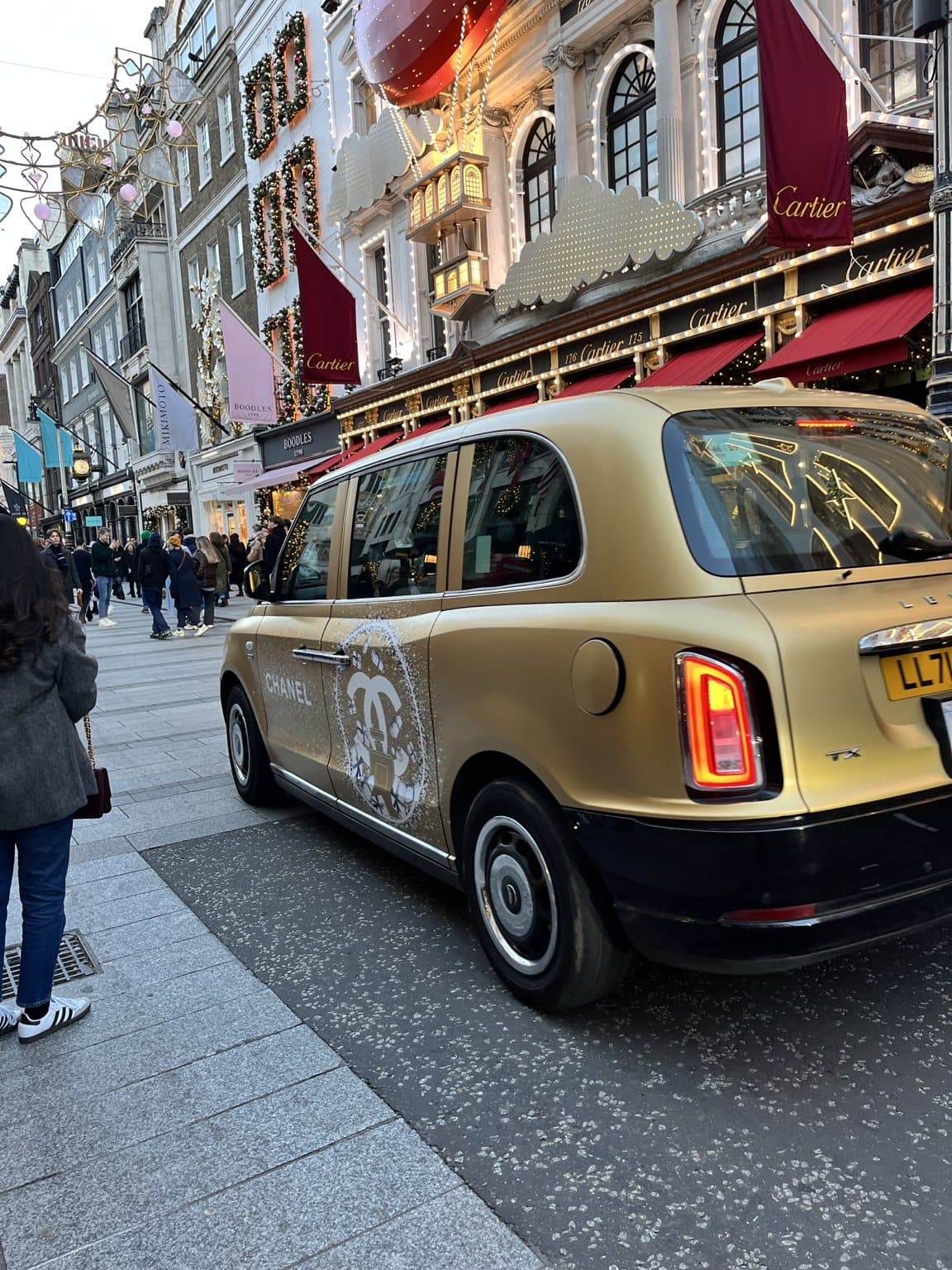 A gold Chanel-wrapped London taxi on Old Bond Street, with the lit-up Christmas façade of Cartier and festive flags behind it.