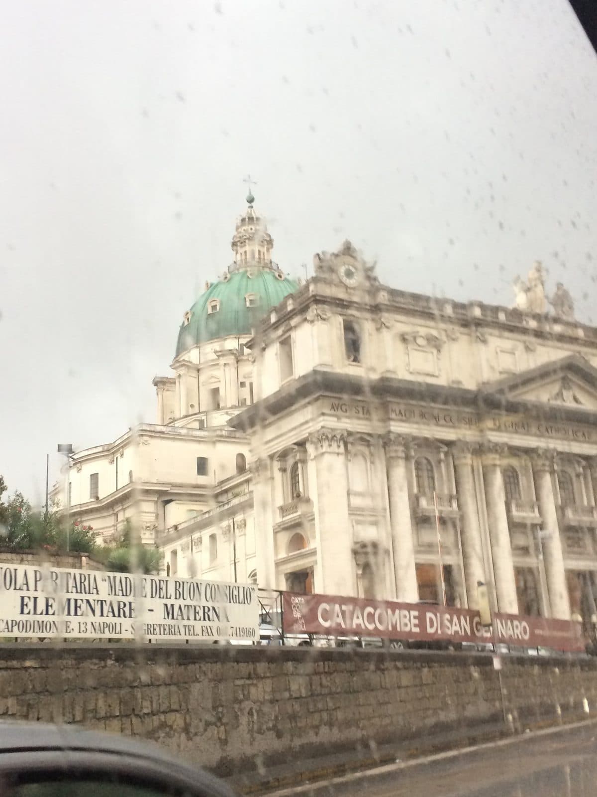 A grand domed church seen through a rain-streaked car window on a grey day in Naples