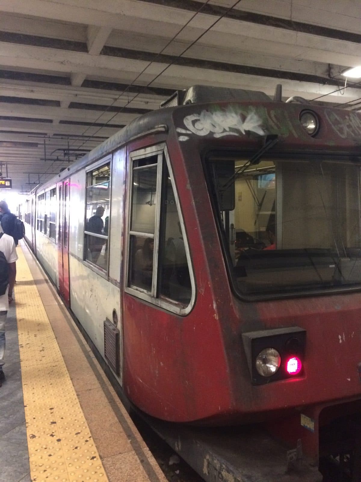 A battered red-and-grey local train standing at a Naples station platform