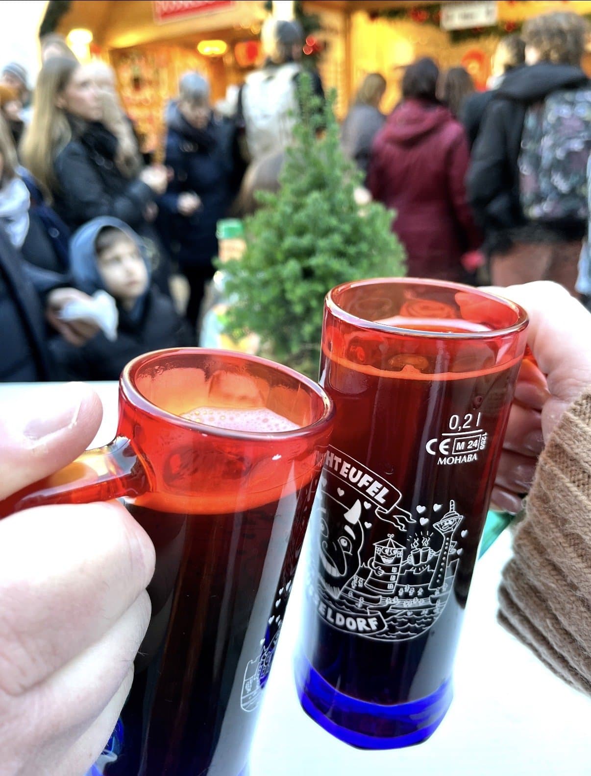 Two mulled-wine mugs printed with Düsseldorf Christmas-market branding, held up at a market stall.
