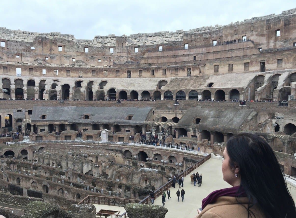 The interior of the Colosseum in Rome, with tiers of ancient arches and visitors walking through.