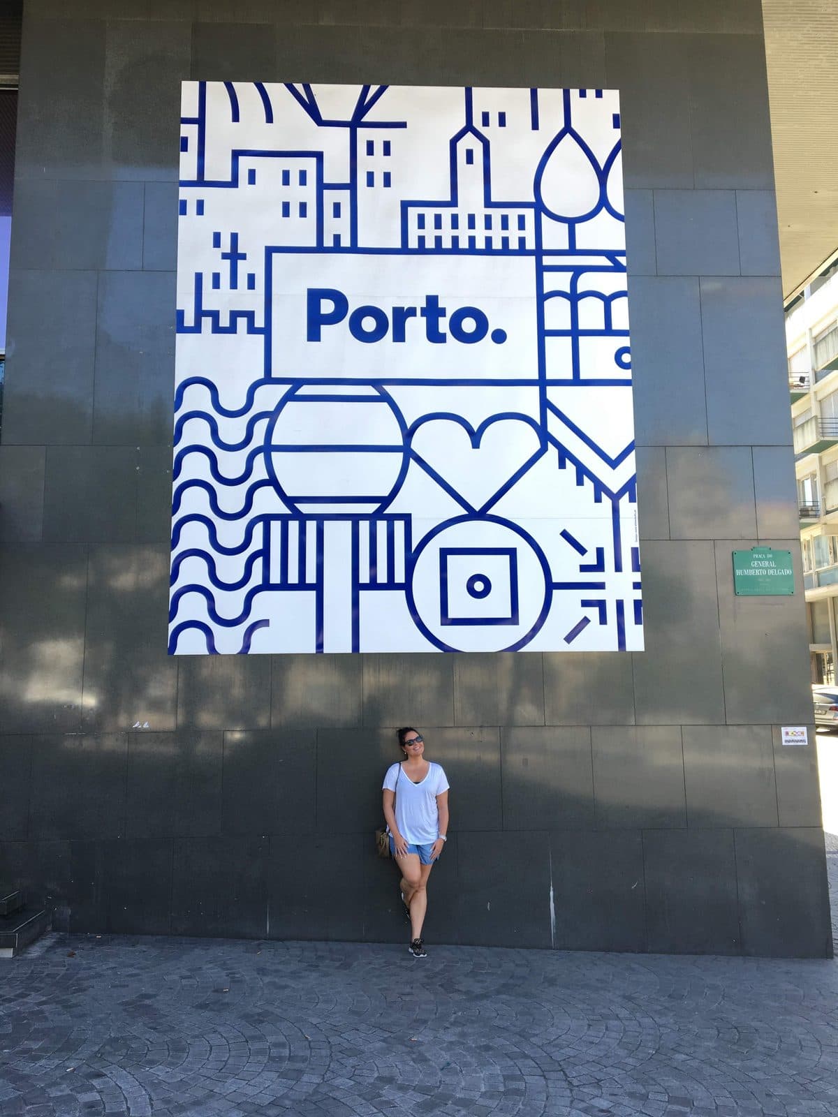 A blue-and-white illustrated “Porto.” city sign on a dark wall, with a small figure standing beneath it