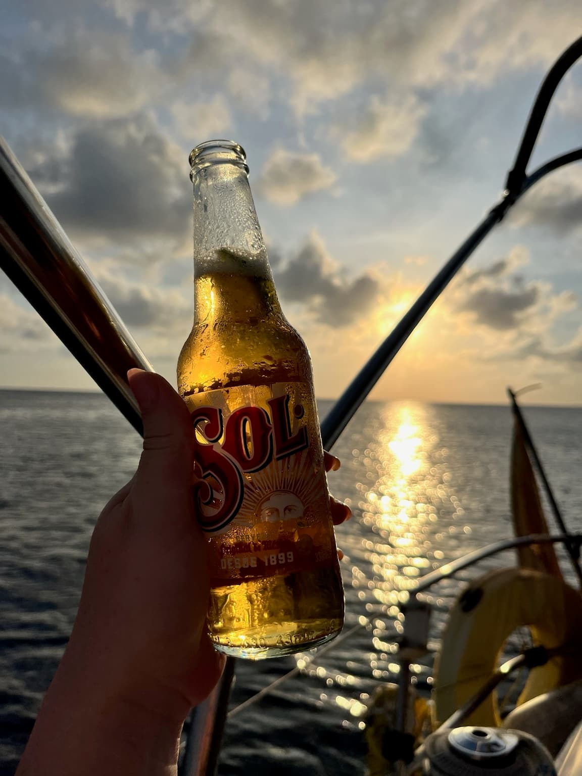 Hand holding a cold beer bottle on a boat with sunlight reflecting across the sea