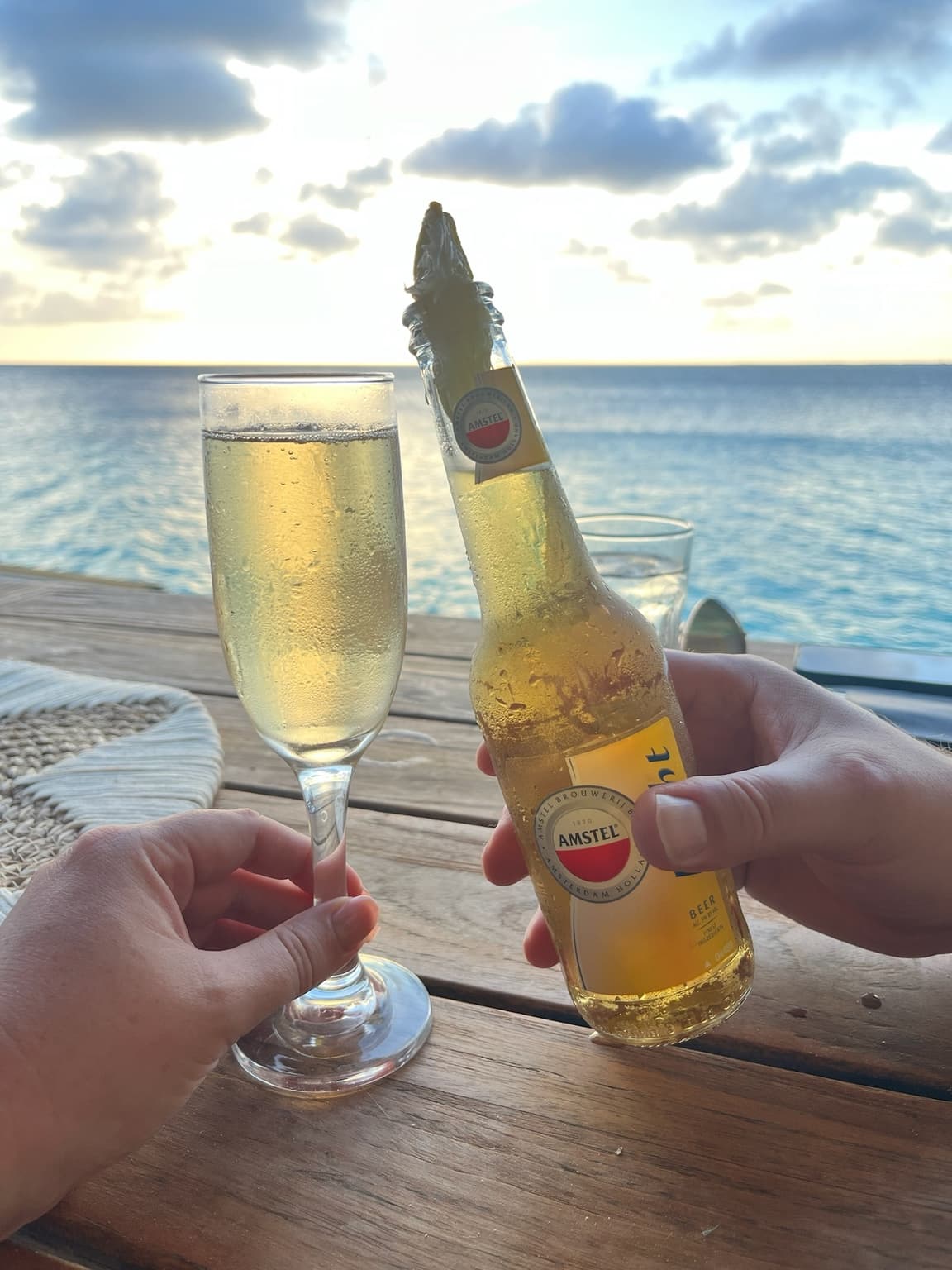 Two hands holding a beer bottle and sparkling-wine glass beside the Caribbean Sea