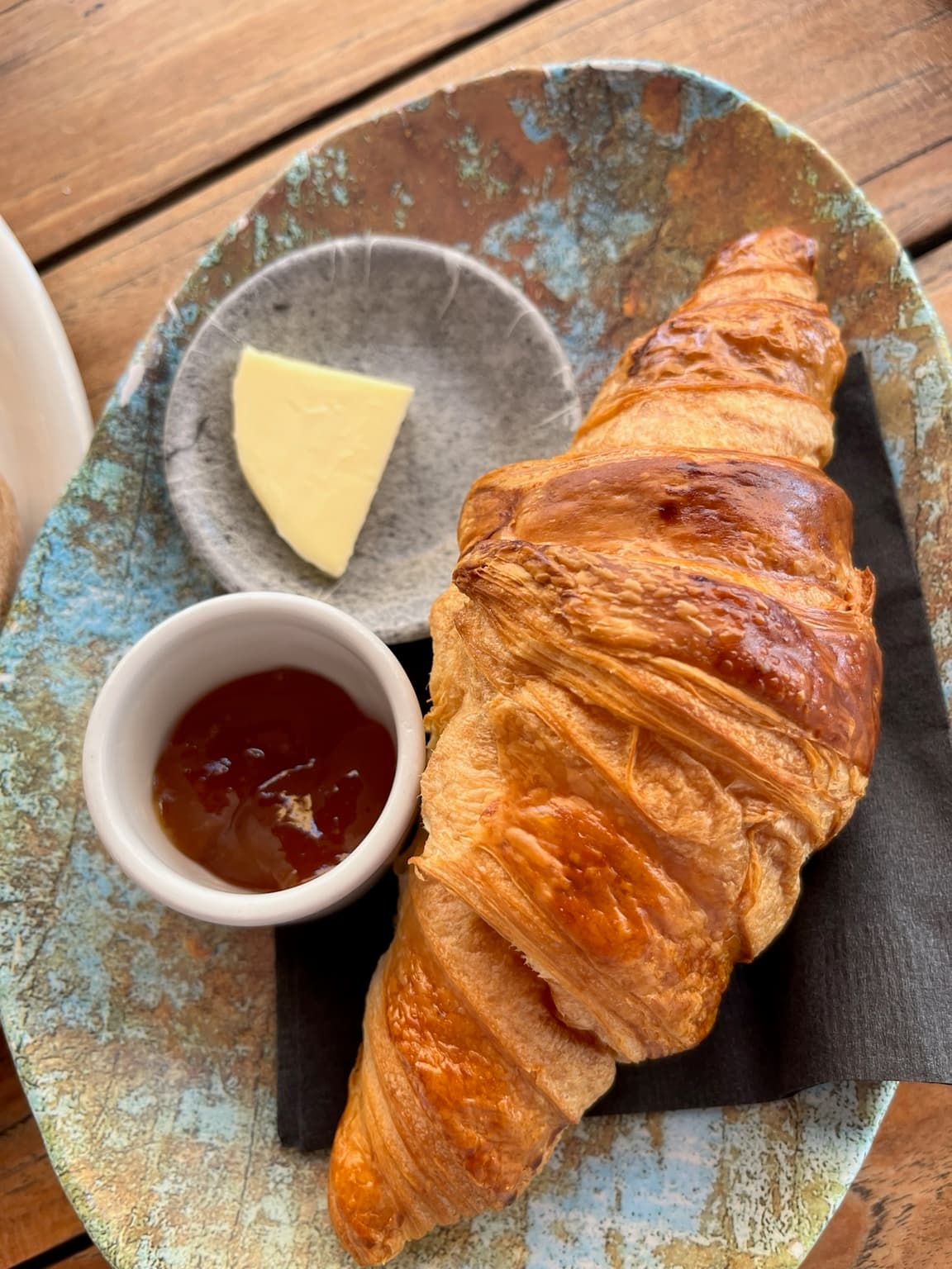 Golden croissant served with butter and preserves on a ceramic plate