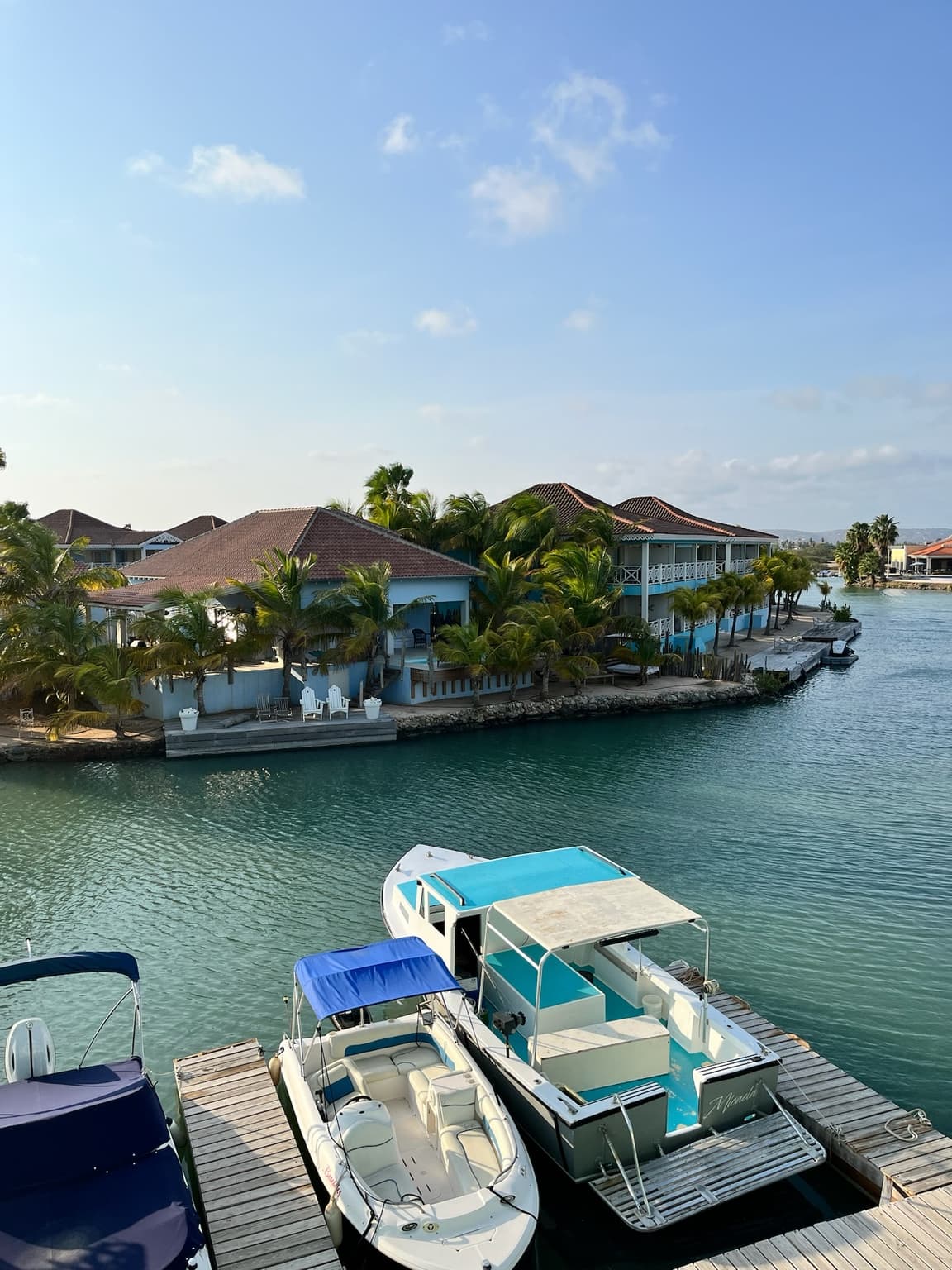Boats moored in a turquoise marina with palm-lined buildings across the water