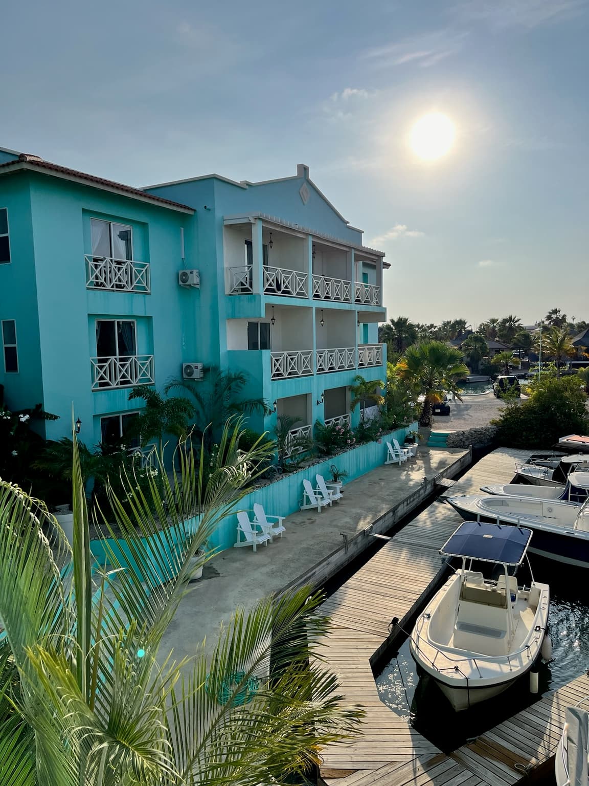 Turquoise hotel building with white balconies beside a marina and palm trees