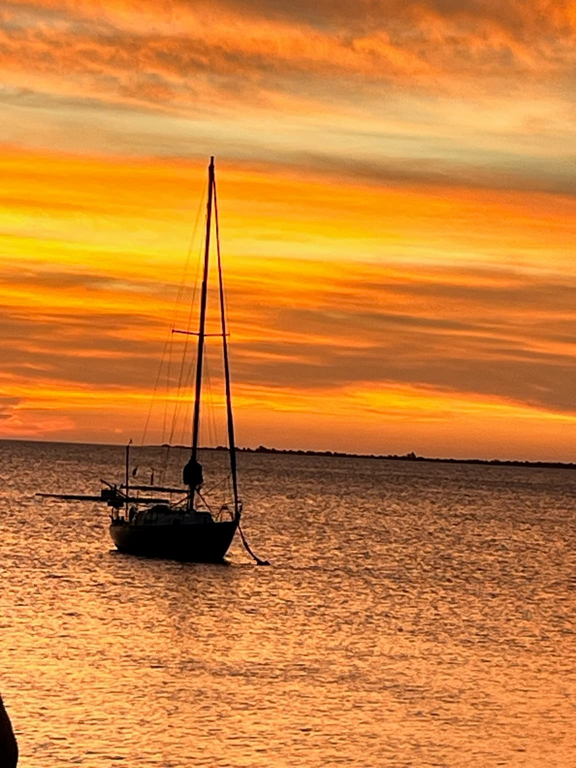 Silhouette of an anchored sailboat against an intense orange sunset over the sea