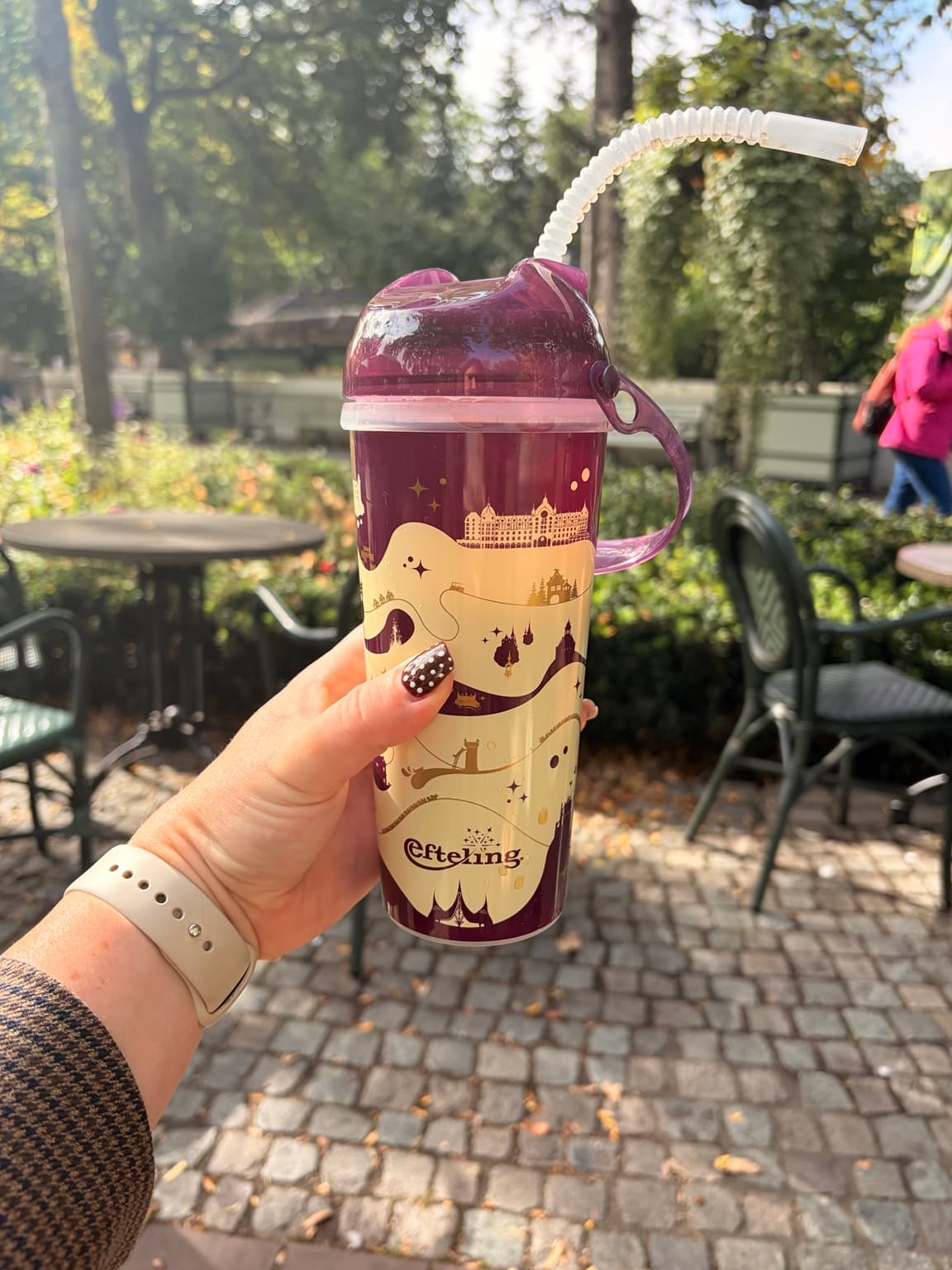 A burgundy and gold Efteling refillable cup held beside an outdoor seating area
