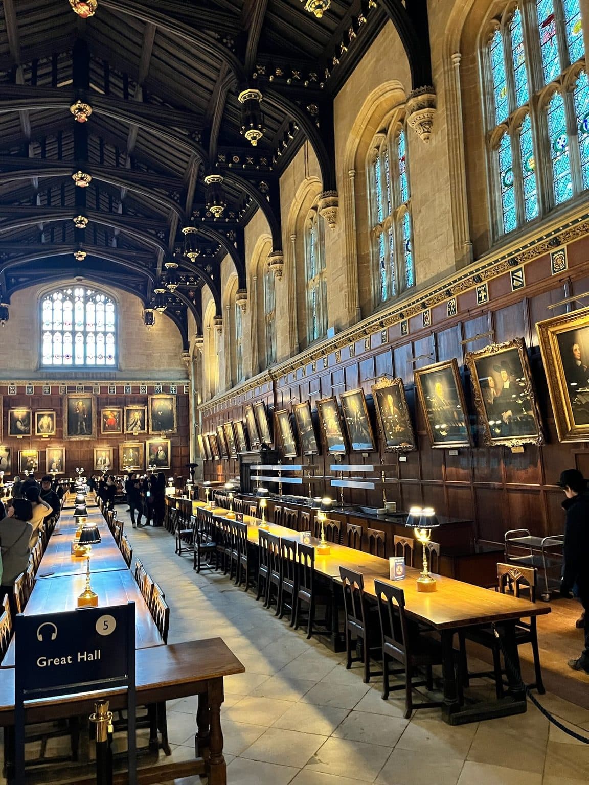 The Great Hall at Christ Church, Oxford: long wooden tables with brass lamps beneath a carved timber ceiling and portraits on panelled walls