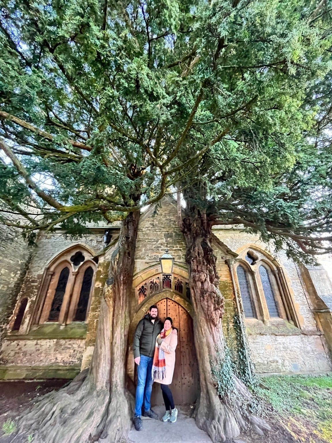 Two people standing at the church doorway framed by yew trees in Stow-on-the-Wold