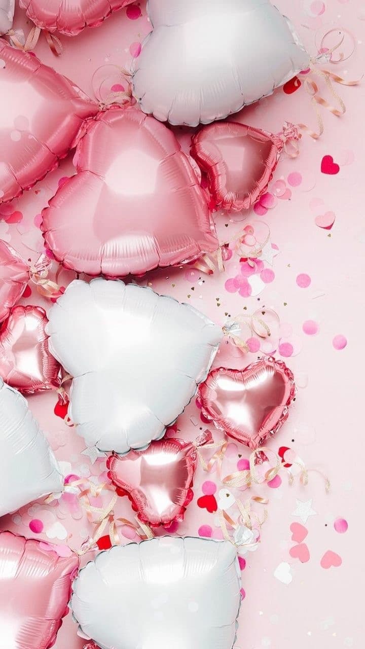 Pink and white heart-shaped balloons with confetti on a pale pink background.